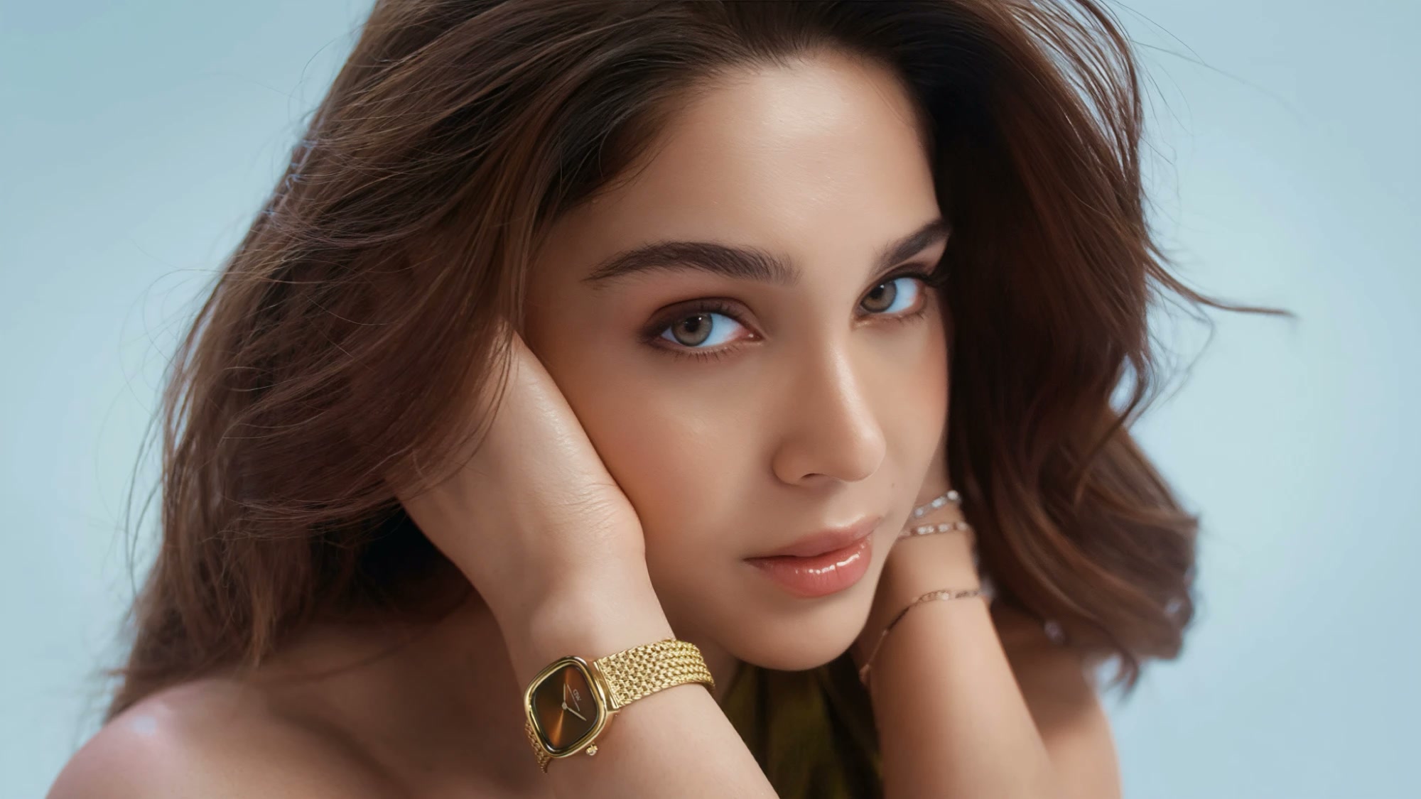 Close portrait with a gold watch on a soft blue backdrop