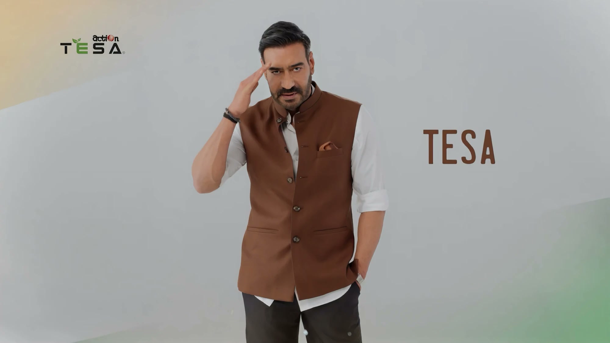 A man in a brown waistcoat gestures near his head against a plain white studio backdrop, beside the TESA logo